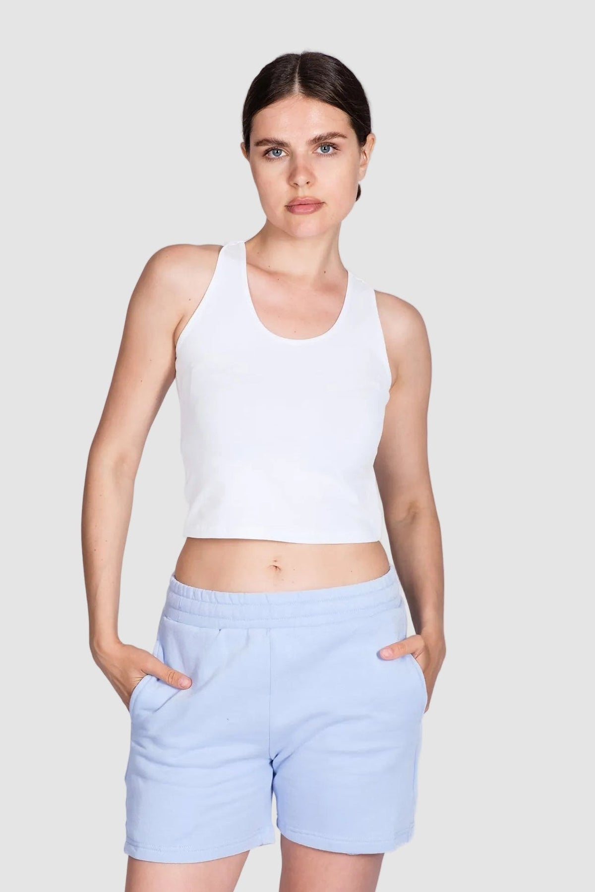 Woman wearing a white tank top and light blue shorts on a white background