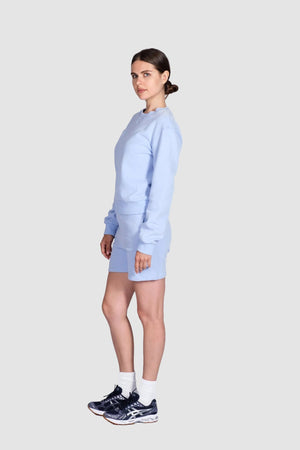 Woman wearing a light blue outfit with black sneakers on a white background