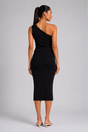 A woman shown from the back wearing a black one-shoulder midi dress and light-colored heeled sandals against a light gray studio background.