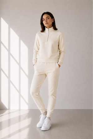 Model with half zip sweatsuit in cream against a beige wall.