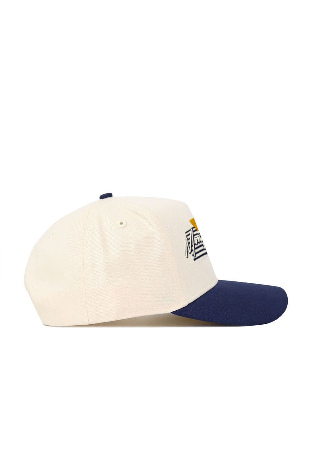 The Montana State Triangle Game Cap Hat is a cream-colored snapback baseball cap with a navy blue brim, made from high-quality cotton. It features an embroidered geometric design with white and yellow accents on the front panel.
