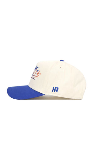 The No Rivals Boise State Triangle Game Cap Hat features a cream crown, blue brim and button, blue NR embroidery on the side, and a multicolored front logo. This structured cap is shown in profile from the left side.