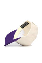 The JMU Triangle Game Cap Hat by No Rivals is shown upside down on a white surface, displaying its inside label. This structured cream-colored snapback features a purple brim.