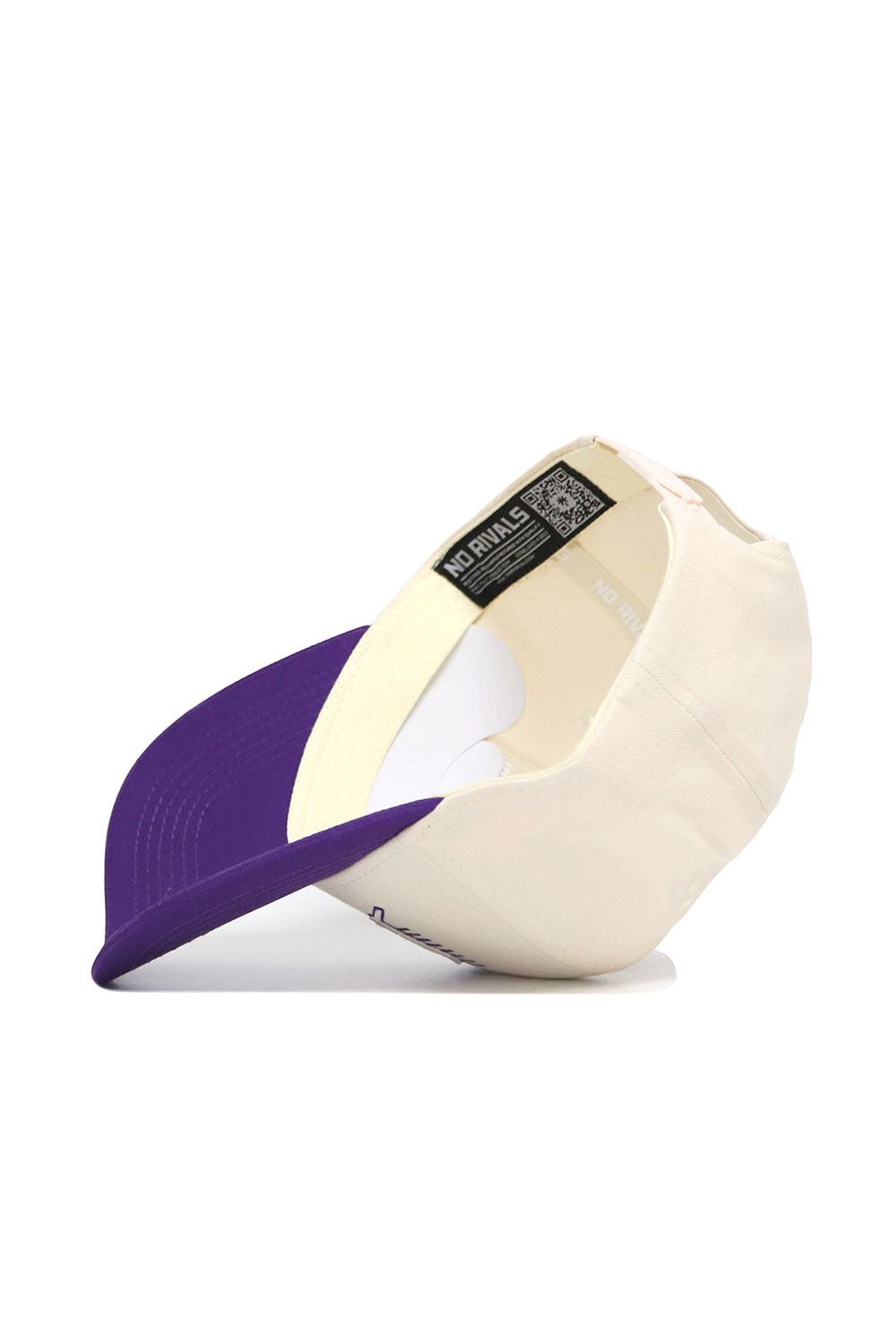 The JMU Triangle Game Cap Hat by No Rivals is shown upside down on a white surface, displaying its inside label. This structured cream-colored snapback features a purple brim.