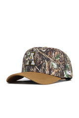 The App State Camo Hat - Explorer Edition is a high-quality cotton camouflage snapback with a brown brim, bold yellow and black "A" on the front, and "NR" in white on the side. Officially licensed, it blends comfort and style.