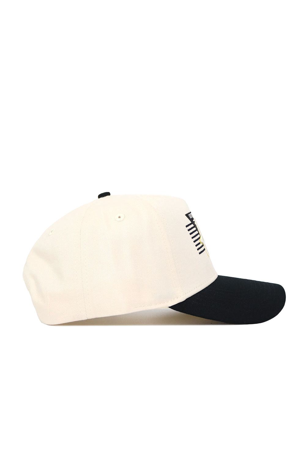 The Iowa Triangle Game Cap Hat by No Rivals is a cream baseball cap with a black curved brim, shown side view. Made from premium cotton, this snapback features subtle vertical black and yellow stripes near the front.