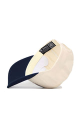 The Liberty Triangle Game Cap Hat by No Rivals is shown from underneath, featuring cream fabric, a navy curved brim, visible inner stitching, an official No Rivals tag, and a QR code on the inside band for authenticity.