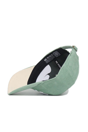 The Iowa Corduroy Hat from No Rivals’ Spring Showers Collection is pictured here in spring green, displayed upside down to reveal the beige underside of the brim and a black interior band featuring the “NO RIVALS” logo. This unstructured 6-panel snapback cap combines casual style and comfort, distinguished by its unique corduroy texture.