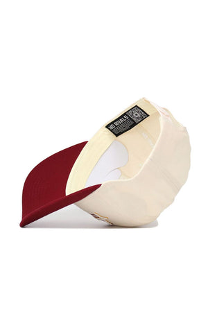 The Iowa State Triangle Game Cap Hat by No Rivals, a cream-colored cotton baseball cap with a maroon brim, is shown upside down to reveal its interior and No Rivals tag. This structured snapback rests on a white surface.