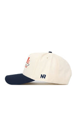 The No Rivals Syracuse Triangle Game Cap Hat is cream with a navy brim, featuring an embroidered NR logo on the side and a front graphic with red lines and white details for a stylish, structured look.