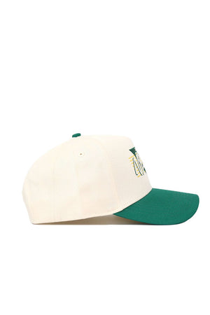 The NDSU Triangle Game Cap Hat by No Rivals is a cream-colored, structured-fit snapback with a green brim, crafted from high-quality cotton. Side view shows embroidered text and graphics partially visible on the front panel.