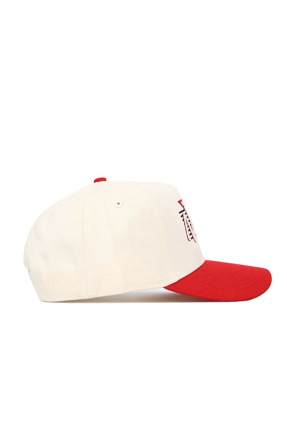 The No Rivals Nebraska Triangle Game Cap Hat is a white snapback with a red brim and top button, shown from the side. Made from high-quality cotton, it features part of a red and white logo on the front.