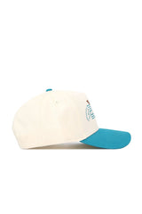 The No Rivals Coastal Carolina Triangle Game Cap Hat is a cream baseball cap with a teal blue brim, shown side view, featuring partial multicolored front embroidery and a structured fit for lasting shape.