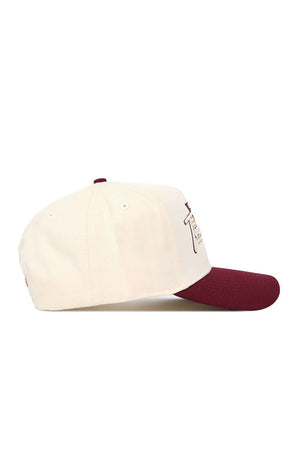 The No Rivals Texas State Triangle Game Cap Hat is a cream baseball cap with a maroon brim, made of high-quality cotton. Seen from the side on a white background, it has stitched eyelets and part of a front design or logo visible.