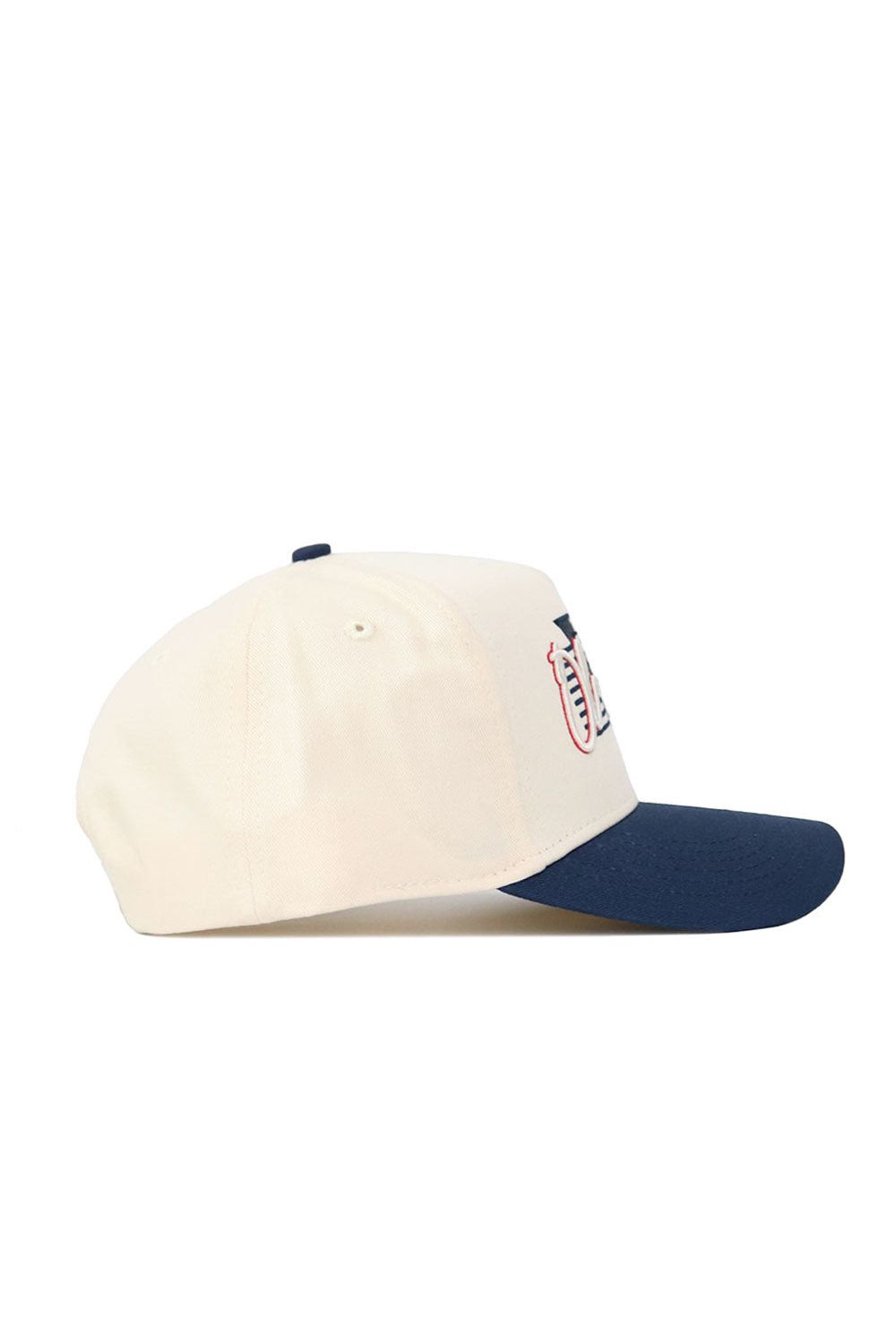 The No Rivals Ole Miss Triangle Game Cap Hat is a cream snapback with a navy blue brim, shown from the side. This structured cap features partial embroidery of a logo on the front.