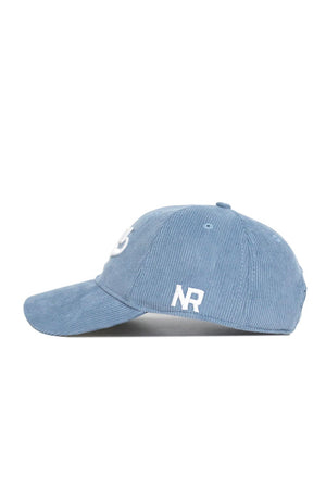 The No Rivals Iowa Corduroy Hat from the Spring Showers Collection is an unstructured 6-panel cap in sky blue, shown from the side. It features a white embroidered NR on the side panel, a curved brim, and an adjustable strap at the back.