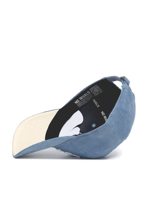 The Iowa Corduroy Hat from No Rivals’ Spring Showers Collection is displayed upside down, revealing its beige underside brim and black inner lining accented with “NO RIVALS” in white. This unstructured, sky blue 6-panel corduroy cap also includes an adjustable strap for a comfortable fit.