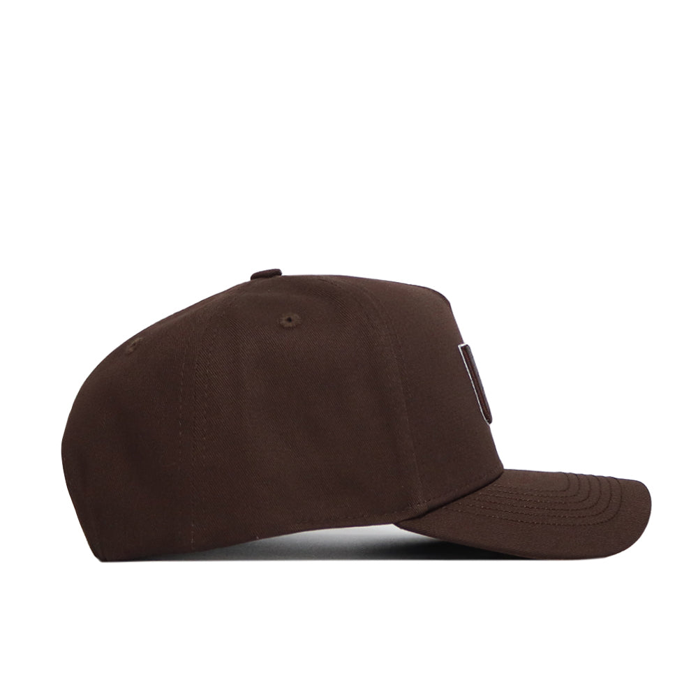 The Miami Hurricanes Americano Hat is a brown, high-quality cotton baseball cap with a curved brim, small top button, and structured fit. Shown from the side against a white background, the hat is plain with minimal details.