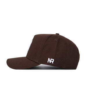 The Syracuse Americano Hat is a brown, structured-fit baseball cap shown from the side. It features white embroidered NR initials near the back, a curved brim, snapback closure, and high-quality cotton with no front logo.