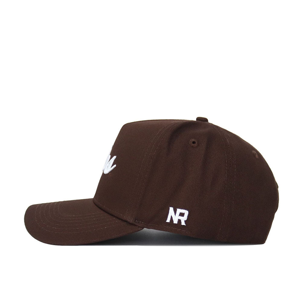 The Western Kentucky Americano Hat is a brown cotton baseball cap with a flat brim, white embroidered NR initials on the side, and a small white front design. It’s shown in side profile against a white background.