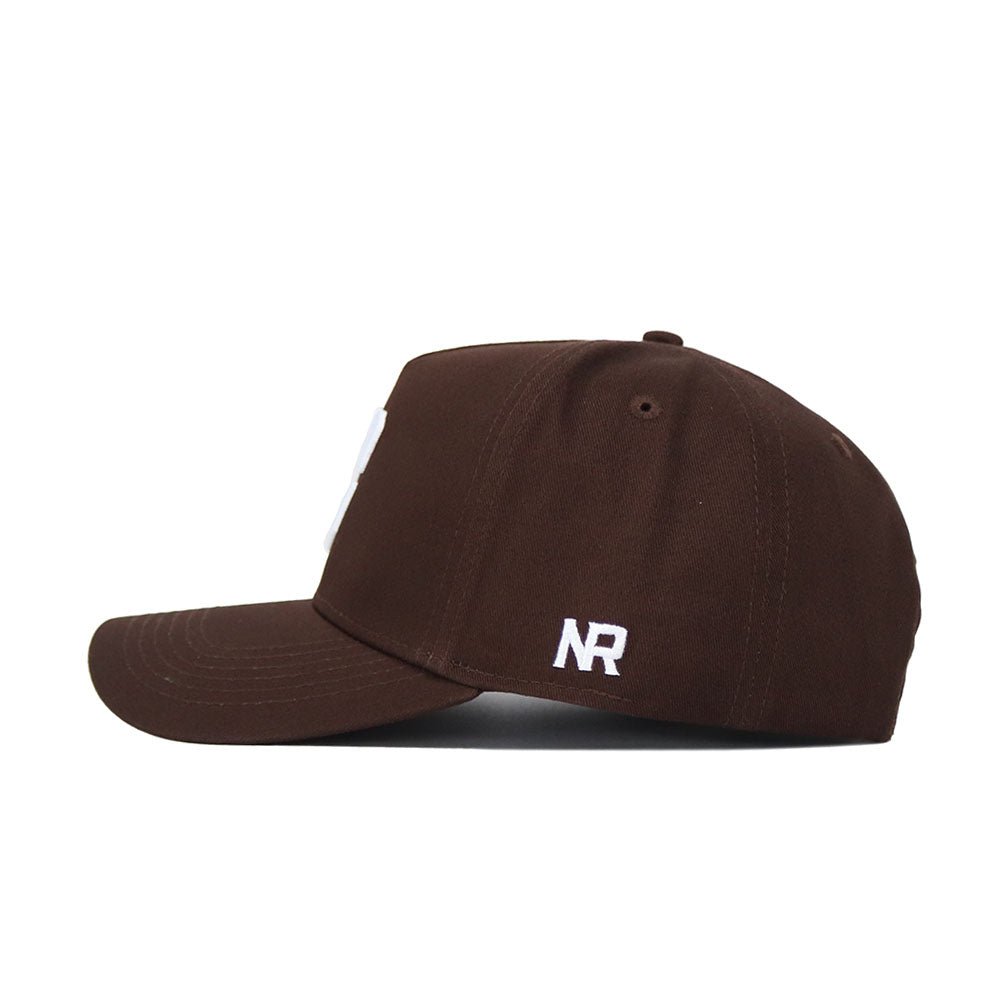 The UNC Charlotte Americano Hat is a brown snapback cap shown from the side, with white NR embroidery near the back. Made of high-quality cotton, it features a curved brim and detailed stitching.