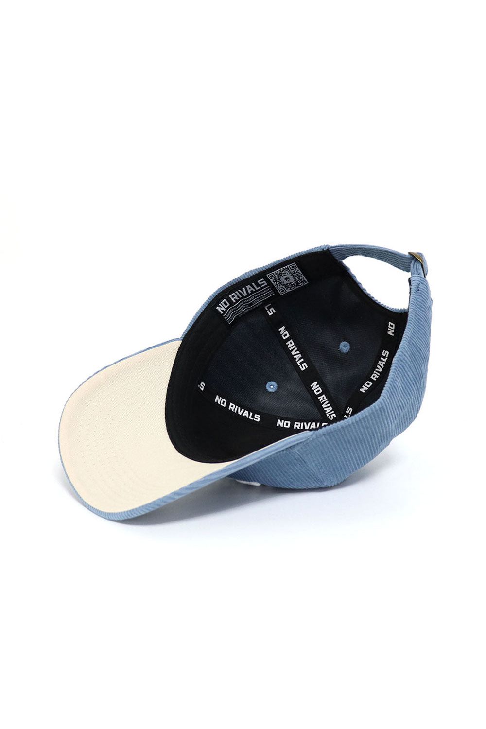 The Dallas Corduroy Hat by No Rivals is an unstructured 6-panel sky blue cap shown from below, featuring a beige inner brim and a black band with repeated white "NO RIVALS" branding.