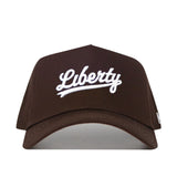 The Liberty Americano Hat is a structured fit brown baseball cap made from high quality cotton, featuring "Liberty" embroidered in white cursive on the front.