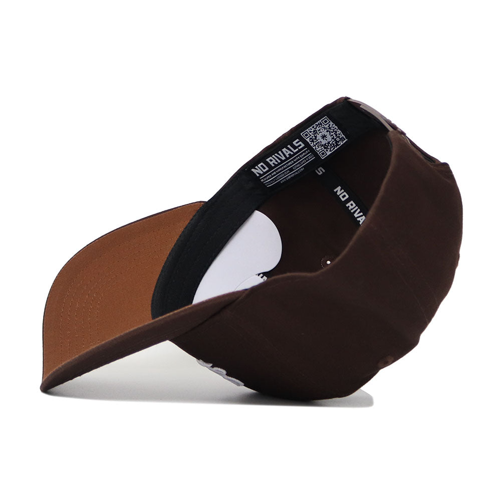 The Liberty Americano Hat, a brown structured fit snapback made from high-quality cotton, is shown on its side, highlighting the curved brim and interior labels that read NO RIVALS.