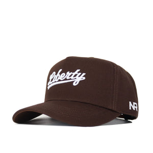 The Liberty Americano Hat is a brown snapback made of high-quality cotton, with "Liberty" embroidered in white cursive on the front and "NR" stitched in white on the left side.