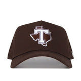 The Tarleton Americano Hat is a brown snapback crafted from high-quality cotton, featuring a structured fit and a bold white "T" centered in an outlined Texas shape on the front.