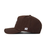 The Tarleton Americano Hat is a brown cotton baseball cap with a structured fit, shown from the side. It features white embroidered "NR" above the back edge for lasting comfort and distinctive style.