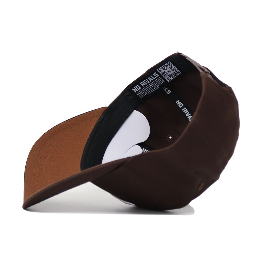 The SMU Americano Hat, a brown high-quality cotton baseball cap, is shown upside down with its black NO RIVALS inner band and part of the white underside visible. The bill faces forward and slightly left.