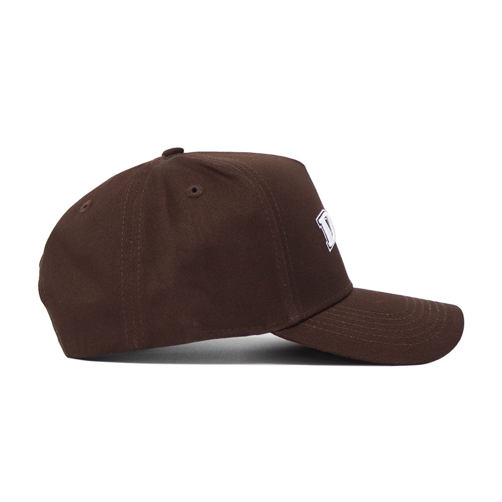 The DBU Americano Hat is a dark brown cotton baseball cap with a curved brim, structured fit, visible side stitching, and an embroidered white logo partially shown on the front.