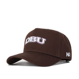 The DBU Americano Hat is a brown snapback featuring "DBU" embroidered in white on the front and "NR" stitched on the left side, made from high-quality cotton for a structured fit.