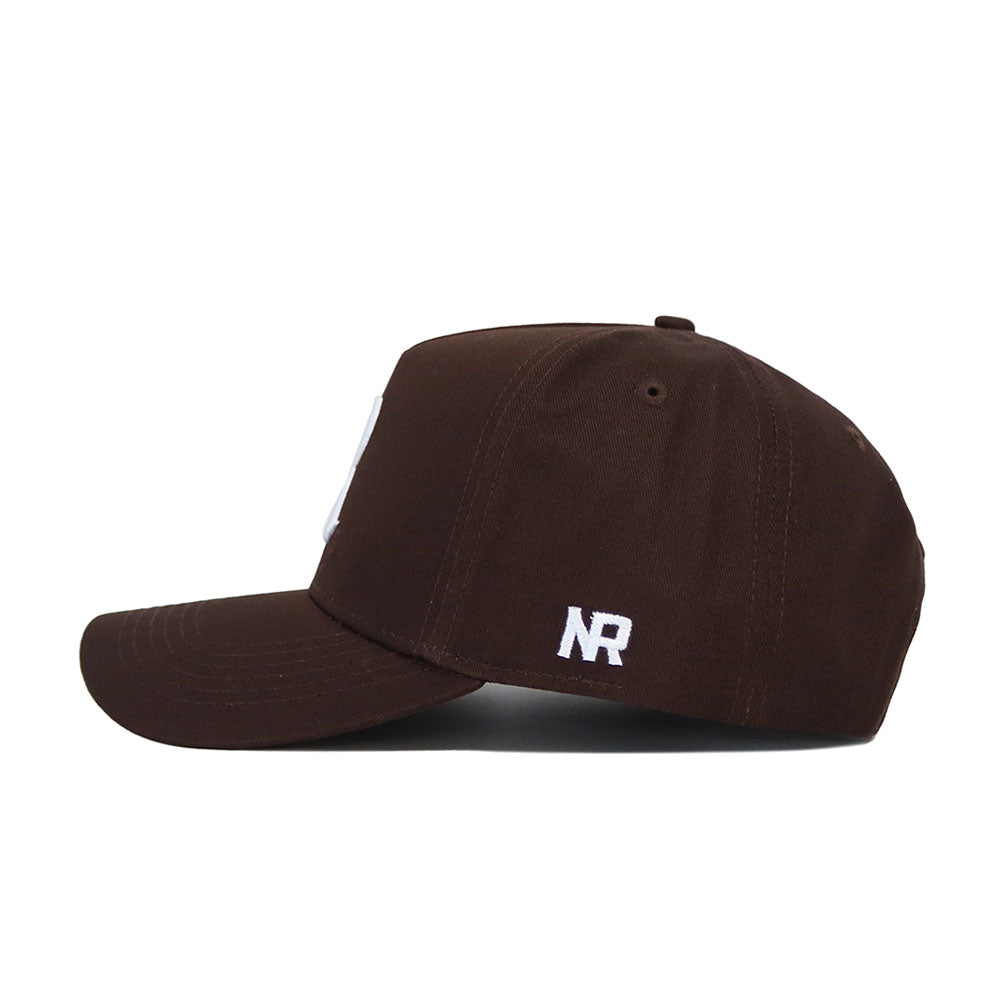 The Rice Americano Hat is a brown baseball cap with white embroidered "NR" near the back, featuring a curved brim, top button, and structured fit for comfort when viewed from the side.