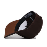 The Rice Americano Hat, a brown baseball cap with a structured fit, is displayed upside down to reveal its inside brim and black sweatband printed with NO RIVALS in white.