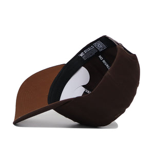 The Rice Americano Hat, a brown baseball cap with a structured fit, is displayed upside down to reveal its inside brim and black sweatband printed with NO RIVALS in white.