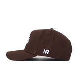 The No Rivals University of Montana Americano Hat is a brown baseball cap with a structured fit, white NR initials on the left side, a partial white front graphic, and is made from high-quality cotton for comfort and durability.