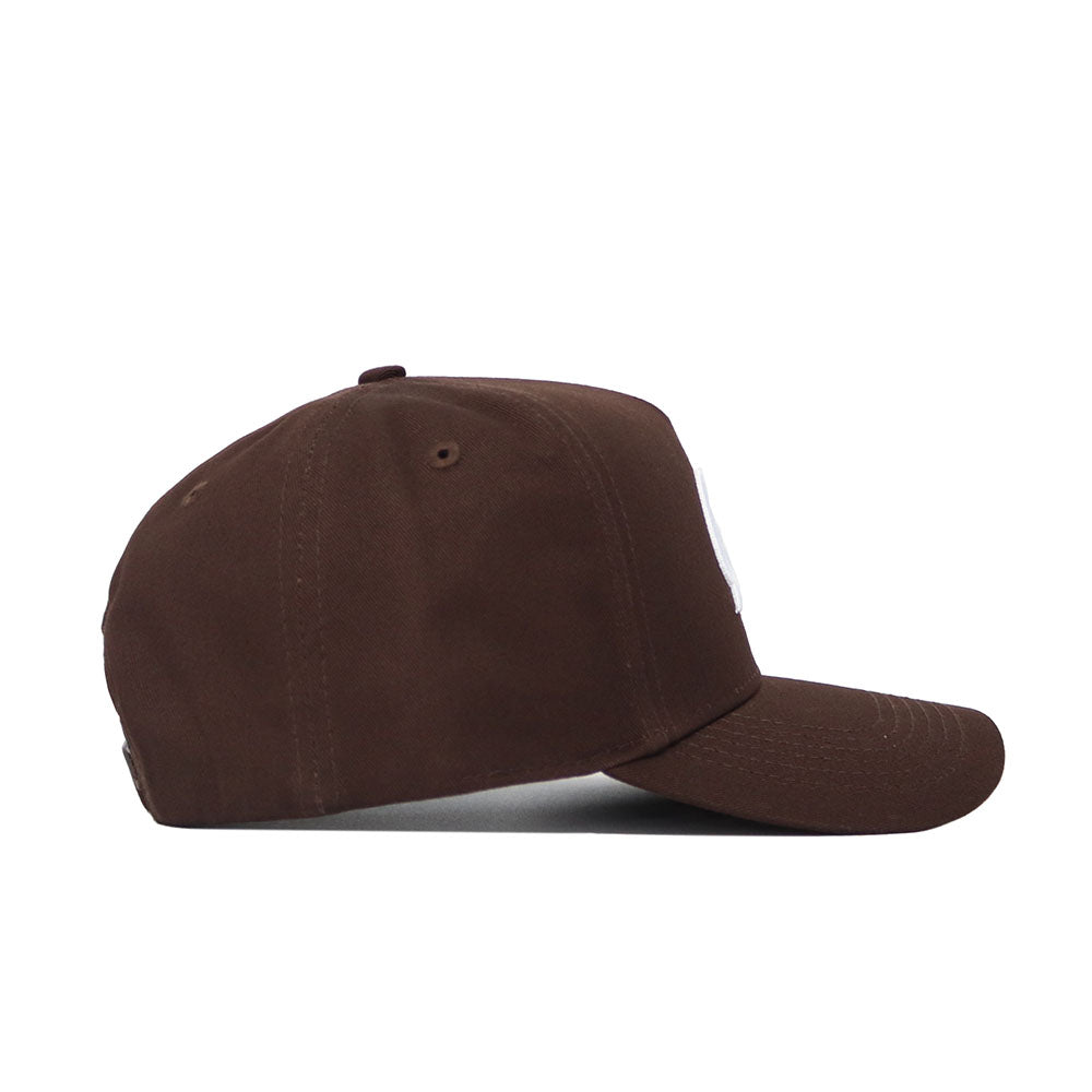The No Rivals University of Montana Americano Hat is a brown, structured snapback with a slightly curved brim, top button, and high-quality cotton. Shown from the side on a white background.