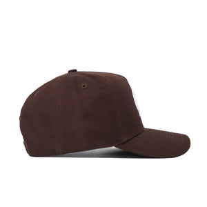 The No Rivals University of Montana Americano Hat is a brown, structured snapback with a slightly curved brim, top button, and high-quality cotton. Shown from the side on a white background.