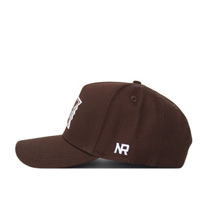 The Hawaii Americano Hat is a brown baseball cap with a flat brim and structured fit, featuring a white NR logo embroidered on the side. The snapback design allows for an adjustable fit. Shown from a side view against a white background.