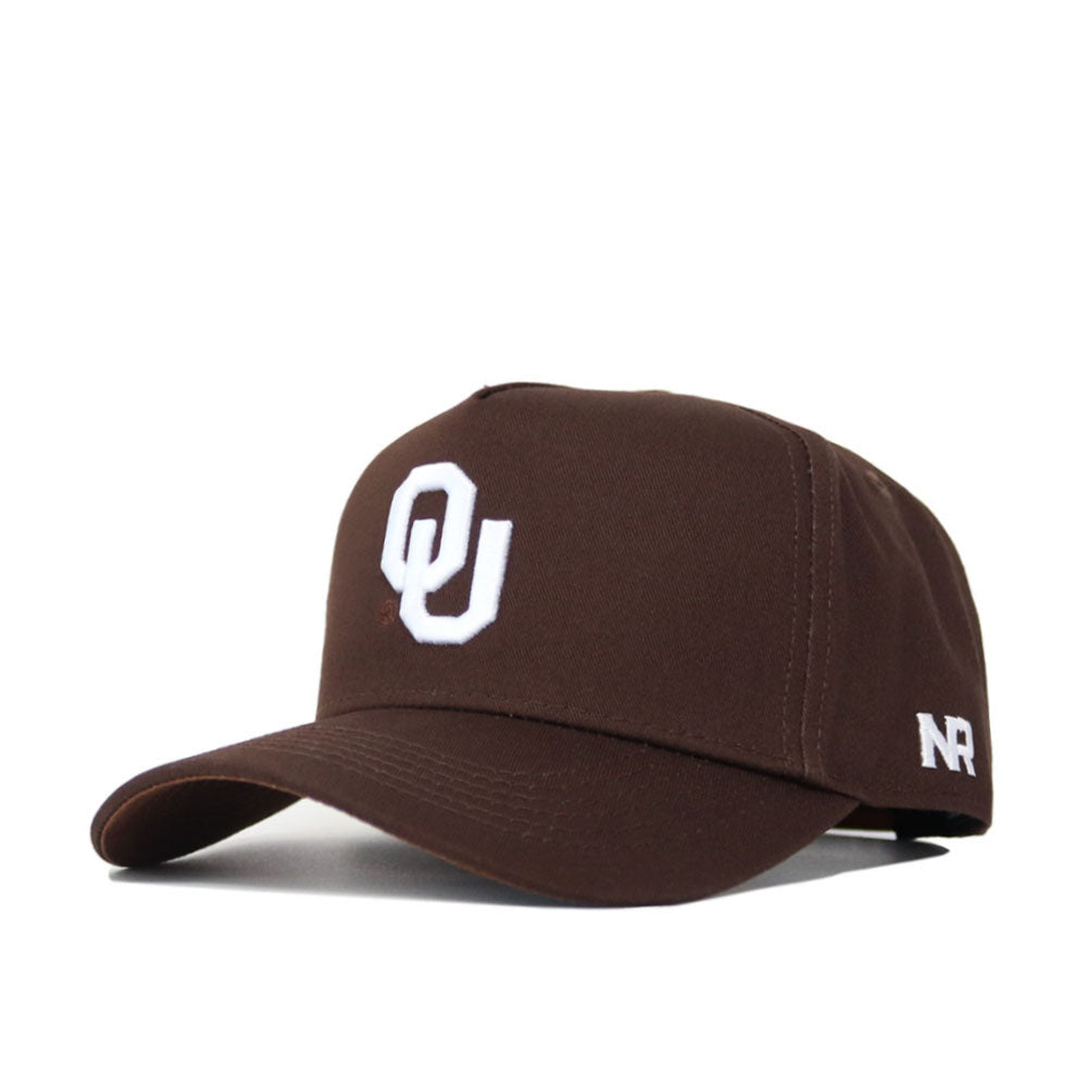 The Oklahoma Americano Hat is a dark brown snapback with a white OU logo on the front and white NR lettering on the side. Made from high quality cotton, it has a curved brim, structured fit, and an adjustable back strap.