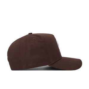 The ECU (East Carolina) Americano Hat is a brown baseball cap, viewed from the side, with a curved brim, structured crown, high-quality cotton fabric, top button, ventilation eyelets, and an adjustable snap back closure.