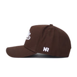The Mississippi State Americano Hat is a brown structured snapback featuring white embroidered lettering on the front, "NR" initials stitched in white on the side, made from high-quality cotton and shown from a left side profile view.