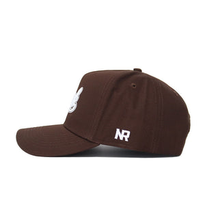 The Nevada Americano Hat is a brown snapback made from high-quality cotton, featuring a white hand peace sign on the front and an embroidered NR on the side, shown in a side profile view.