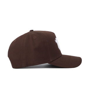 The Nevada Americano Hat is a brown snapback with a flat brim and partial white embroidery on the front panel. Made from high-quality cotton in a structured fit, it's showcased from the side against a plain white background.