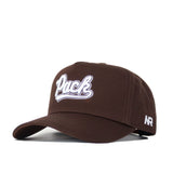 The Nevada Americano Hat is a brown snapback with "Pack" embroidered in white on the front and "NR" on the side. Made from high-quality cotton, it features a curved brim, structured fit, and adjustable back strap.