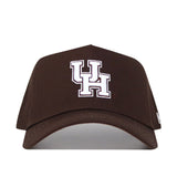 The Houston Americano Hat is a brown baseball cap with a white UH logo, made from high quality cotton. It features a structured fit, classic snapback closure, and is shown against a white background.