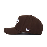 The Iowa Americano Hat is a brown, high-quality cotton snapback with a flat brim. It features white embroidered NR initials on the side and a partial white design on the front, shown against a plain white background.