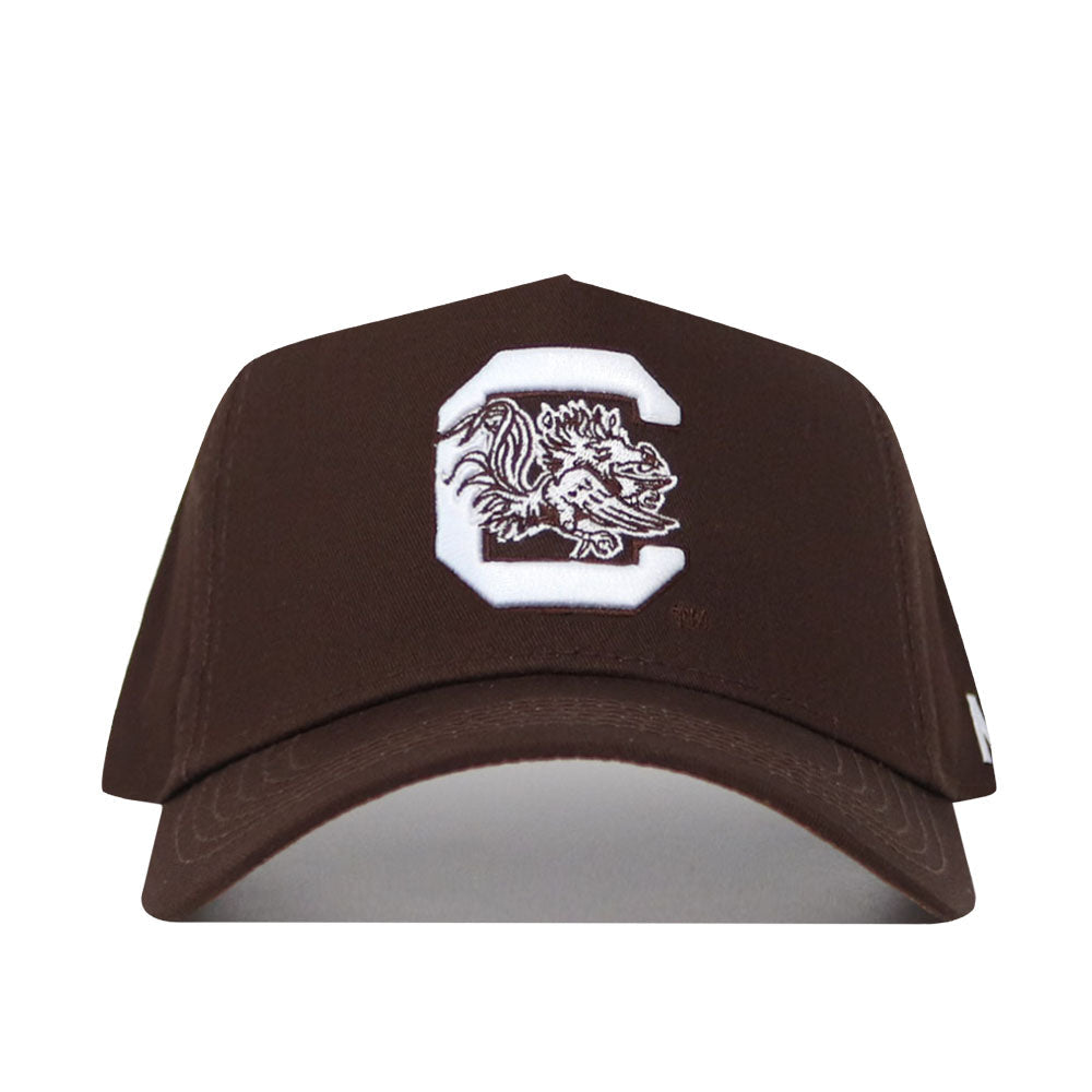 The South Carolina Americano Hat is a brown snapback with a large white "C" and detailed gamecock mascot embroidered on the front. Made from premium cotton, this structured cap offers lasting comfort and classic style.